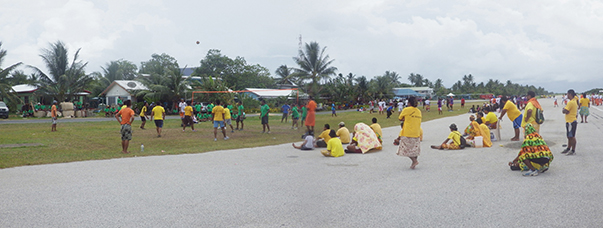 Spectators sit on the runway to watch competitive volleyball teams play on the grass nearby.